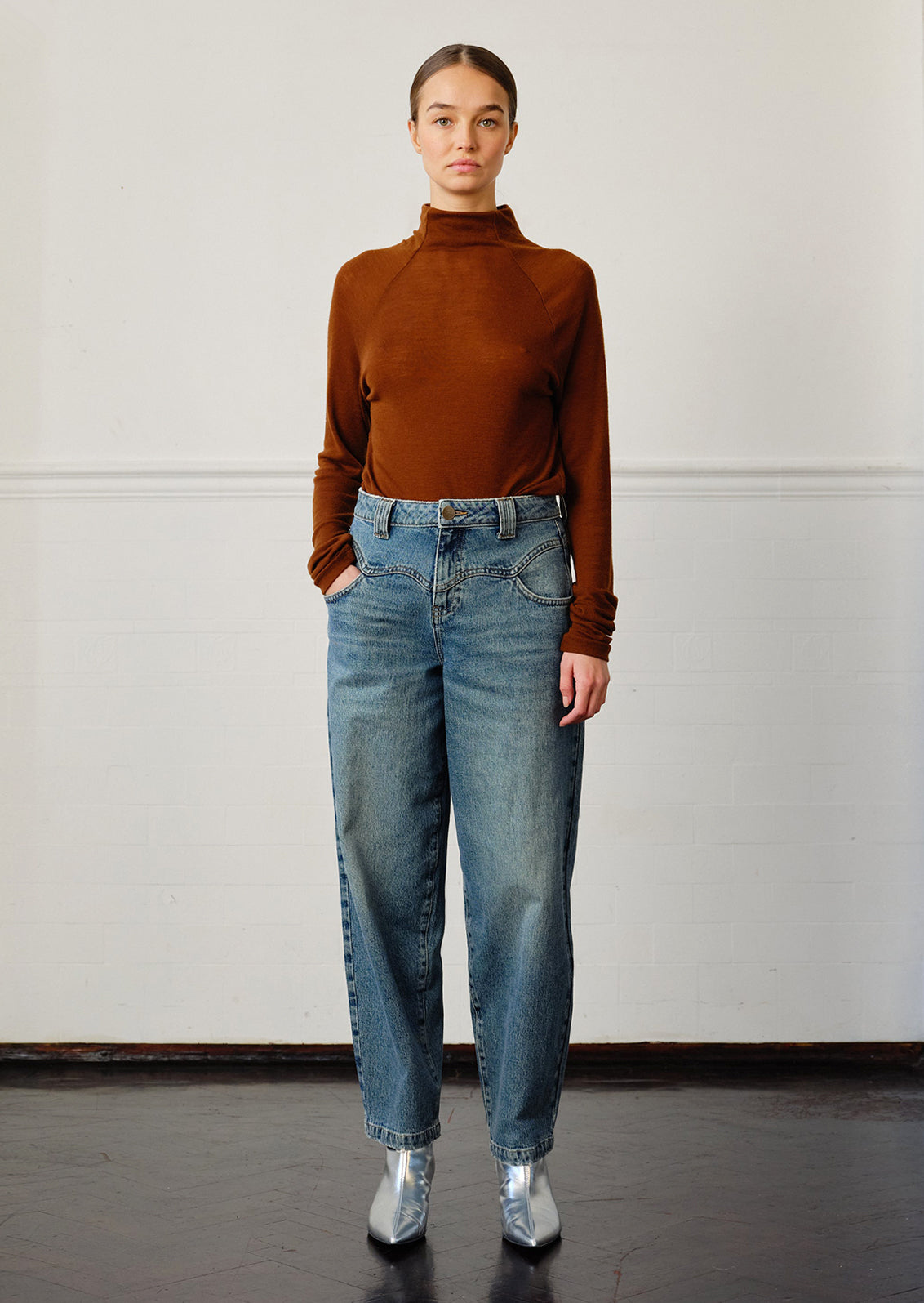 A woman wearing a pair of medium blue denim barrel leg jeans with decorative yoke detailing.