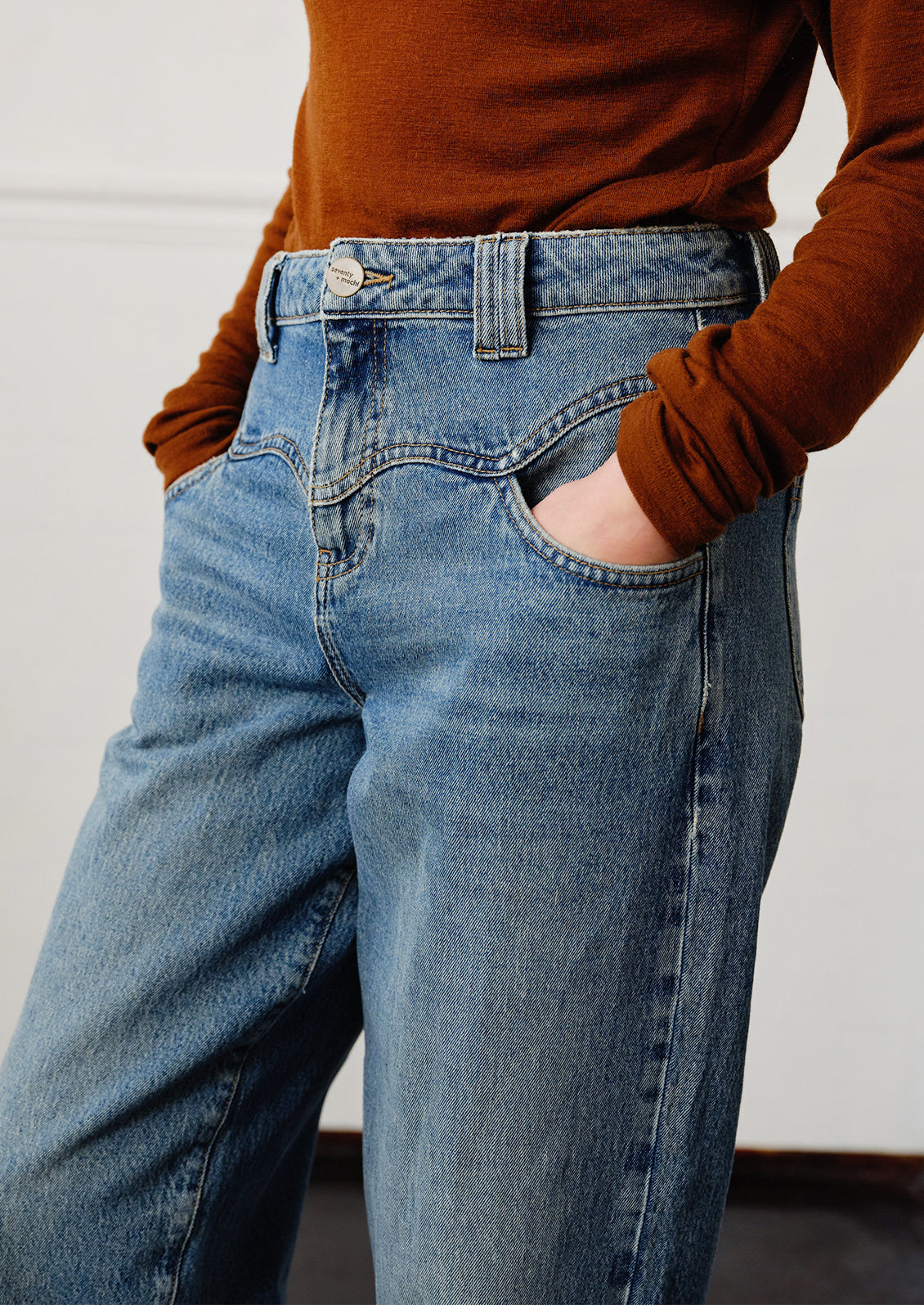 A woman wearing a pair of medium blue denim barrel leg jeans with decorative yoke detailing.