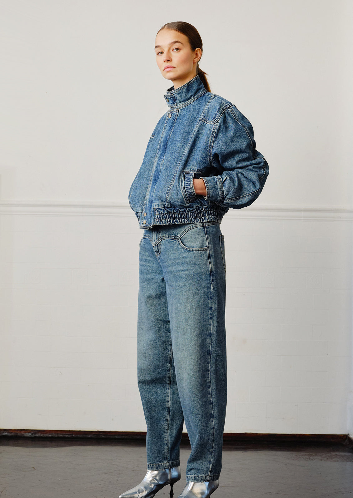 A woman wearing a pair of medium blue denim barrel leg jeans with decorative yoke detailing.