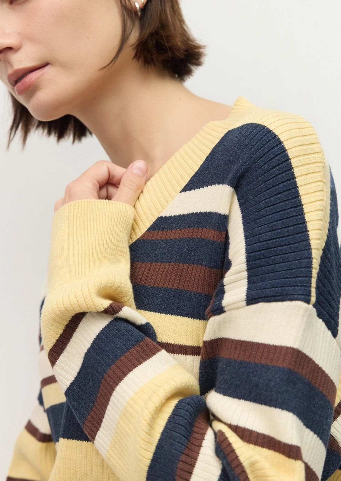 Close-up of a person wearing a ribbed knit sweater with wide horizontal stripes in pale yellow, navy blue, cream, and brown.