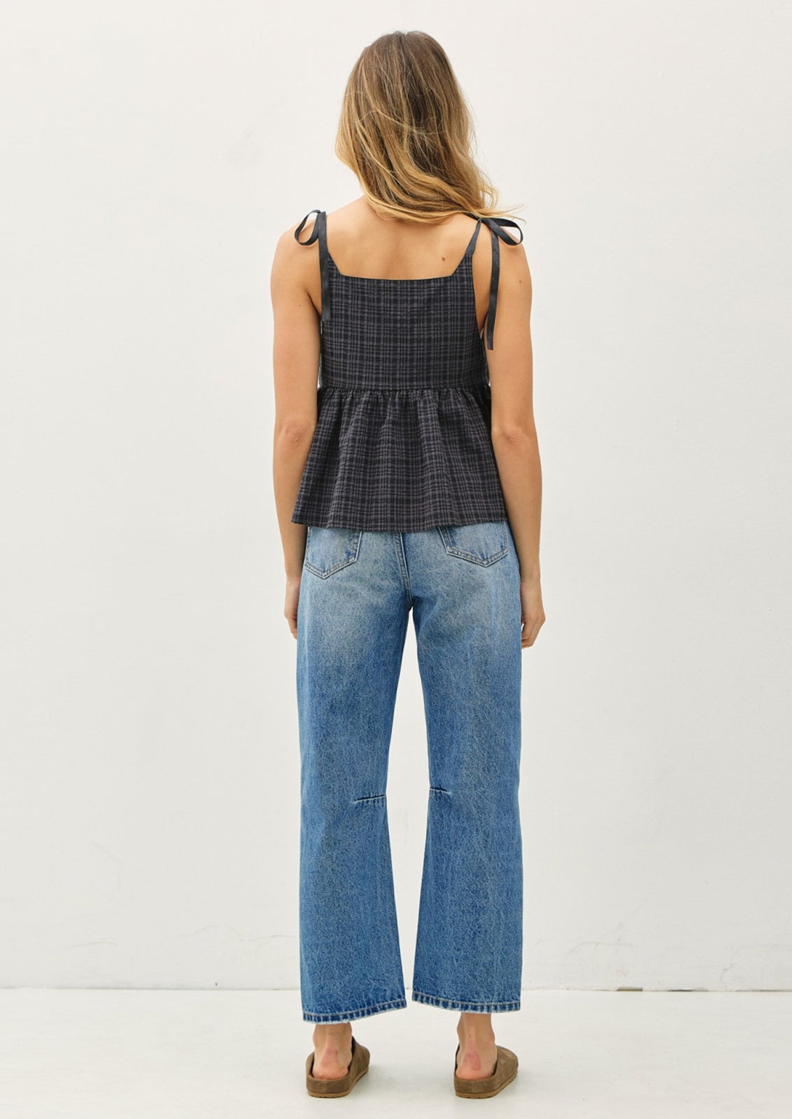 Woman wearing a black checkered top and blue jeans on a white background
