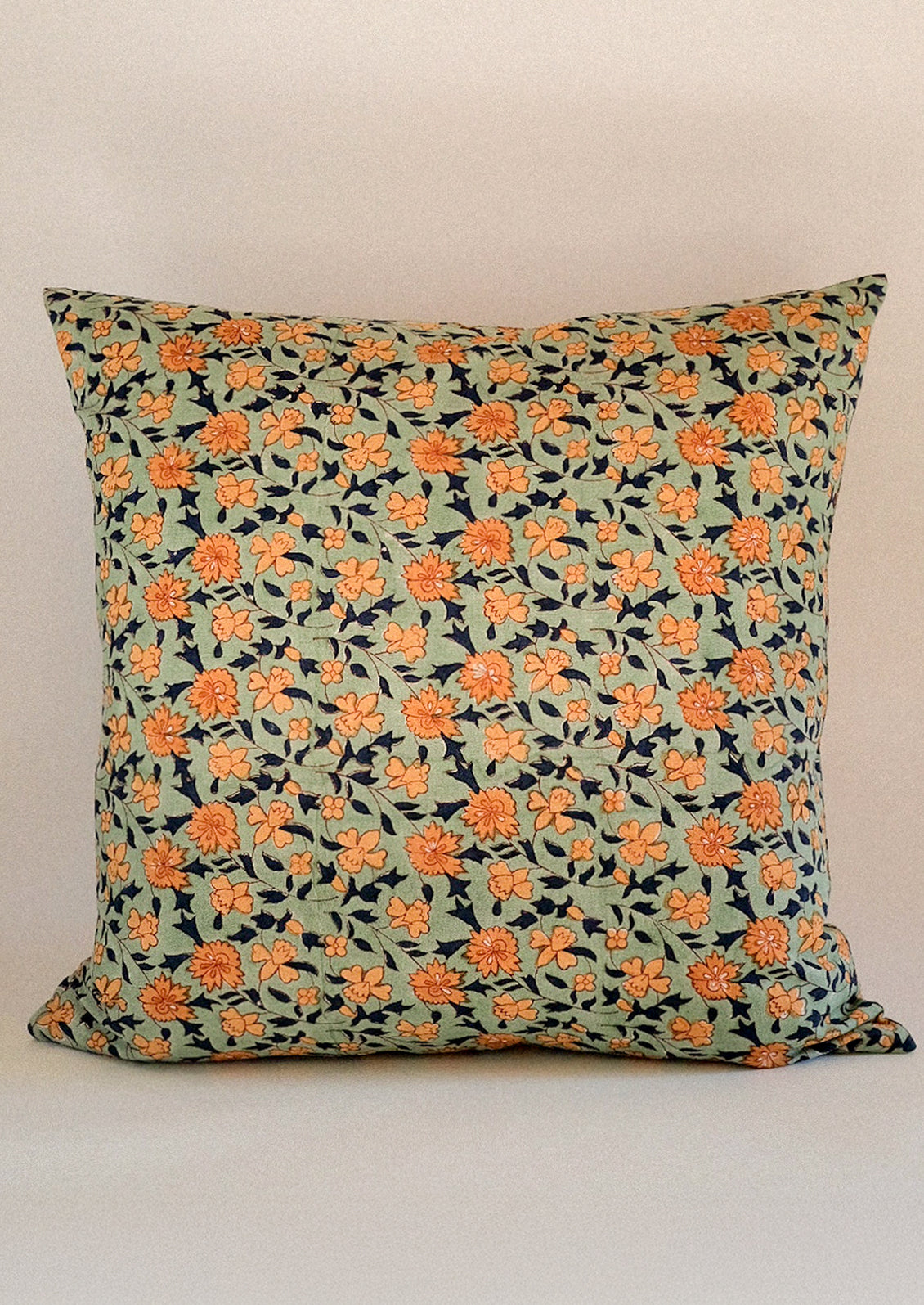A throw pillow in minty green with orange and navy floral pattern.