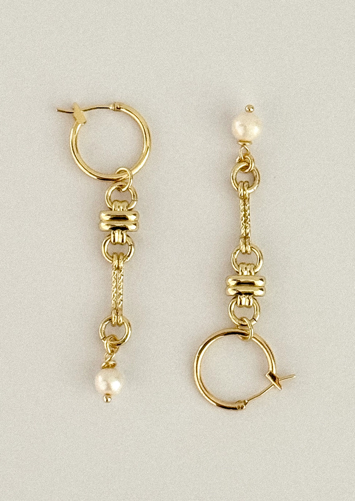 A pair of gold dangle earrings with textured chain links, small pearl-like beads, and circular hoop elements, displayed on a neutral light gray background.