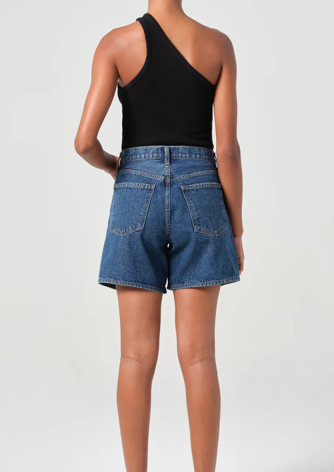 A person wearing a pair of relaxed denim shorts in dark blue wash.