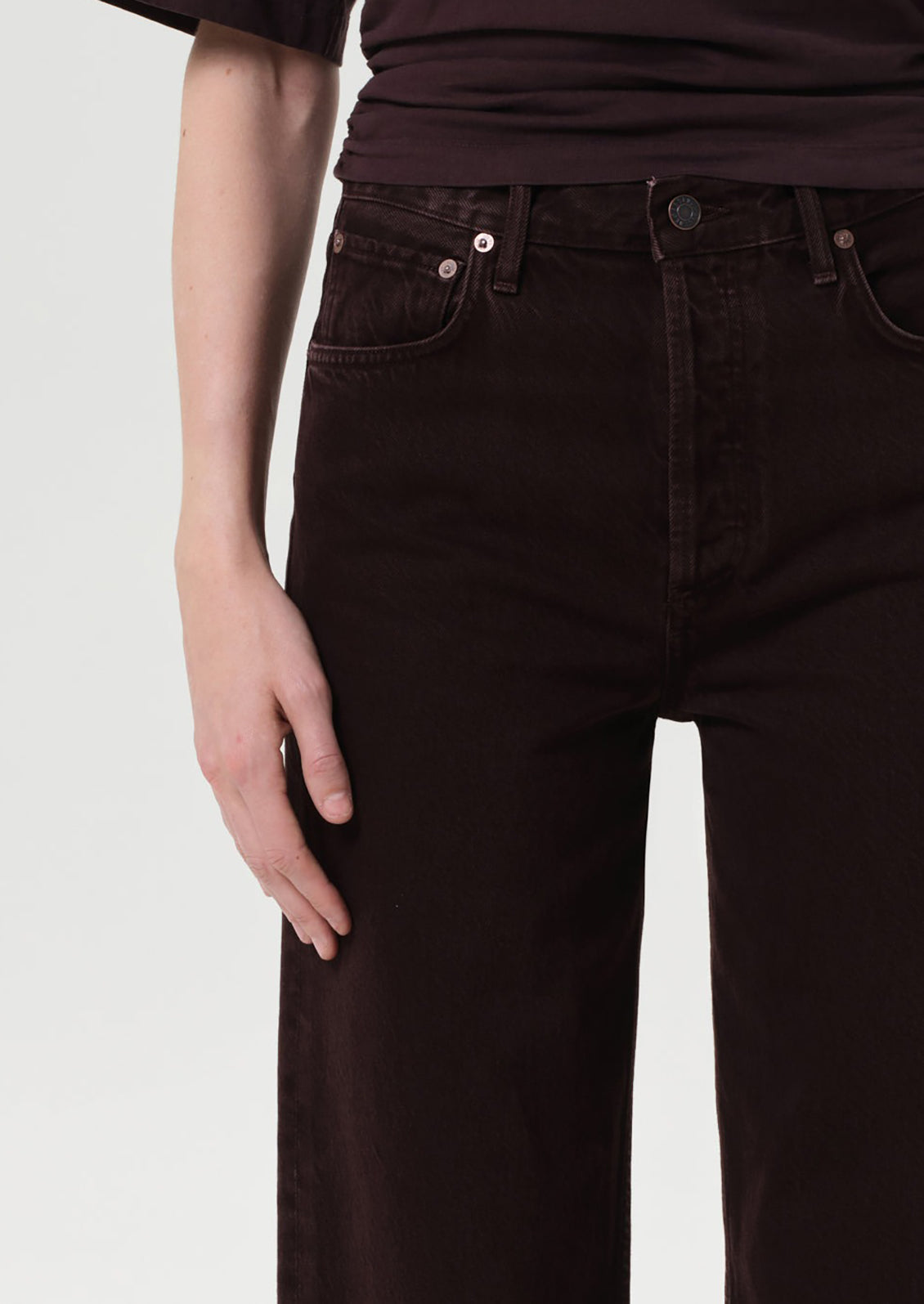 Person wearing dark brown jeans on a light gray background