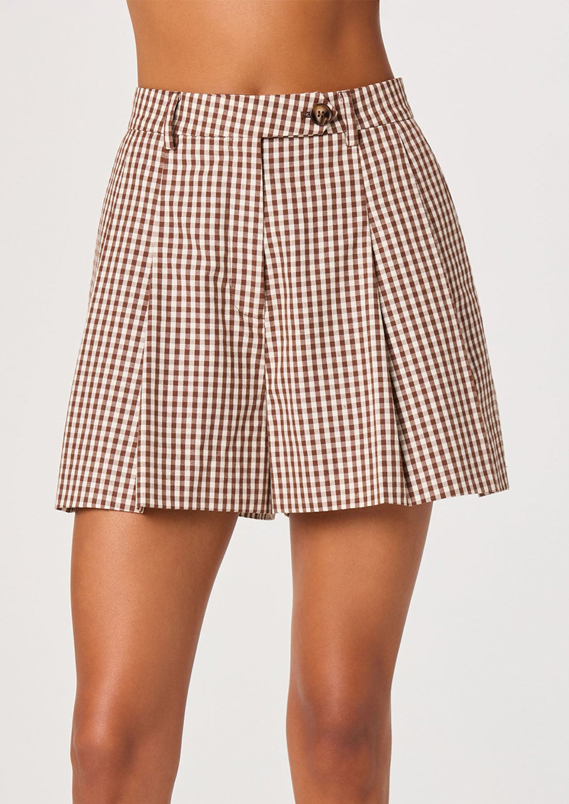 A person wearing a pair of pleated shorts in brown and white gingham.