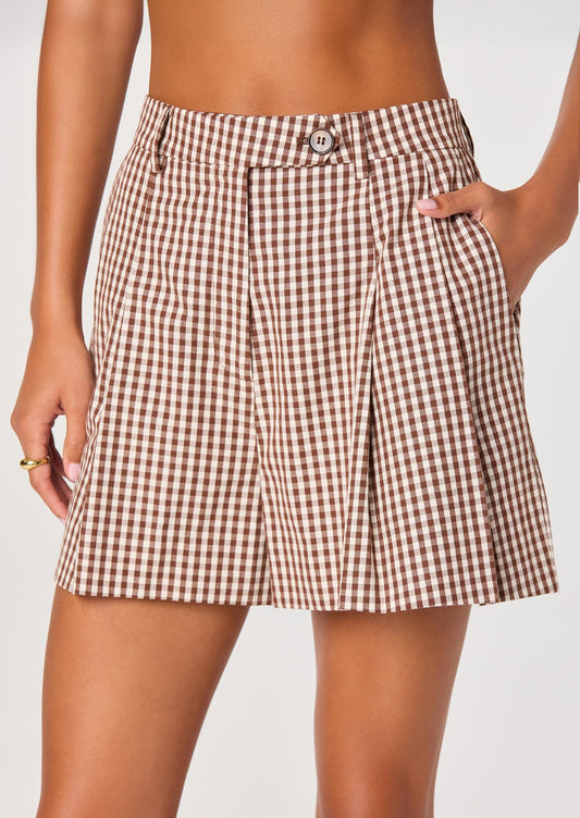 A person wearing a pair of pleated shorts in brown and white gingham.