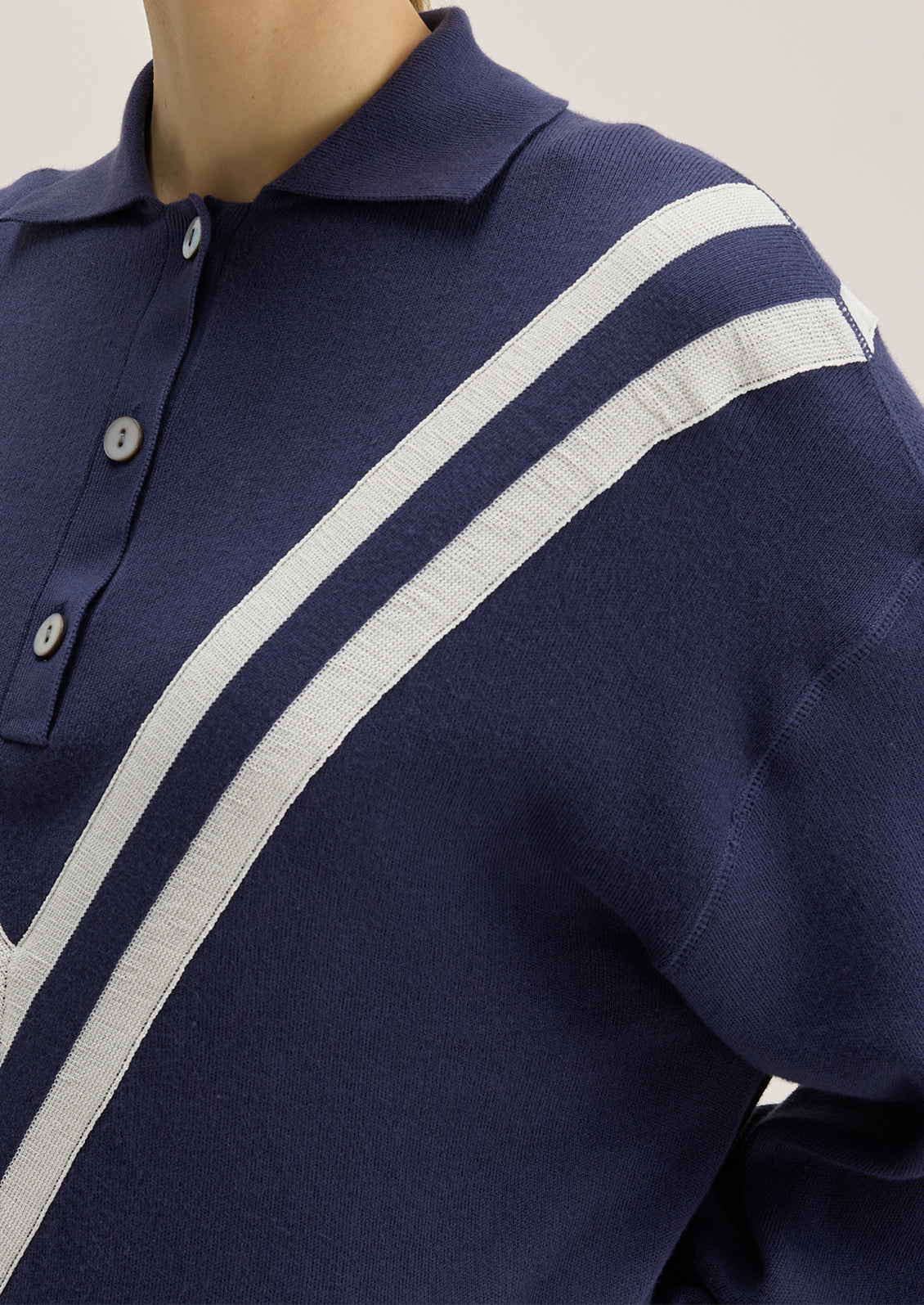 A woman wearing a navy blue henley long sleeve polo with inset V-shaped contrast detailing.