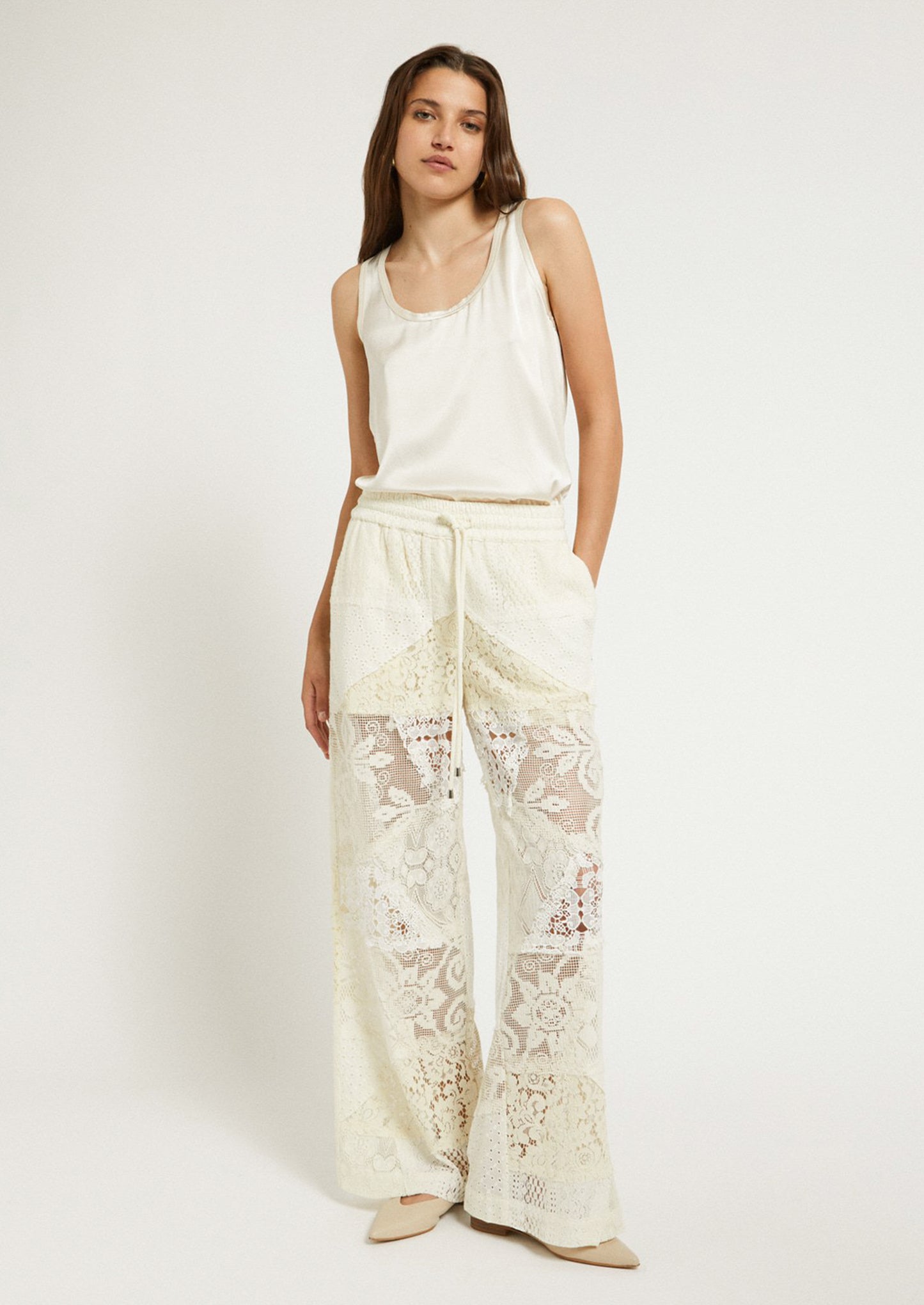 A woman wearing a pair of patchwork lace pants in cream.