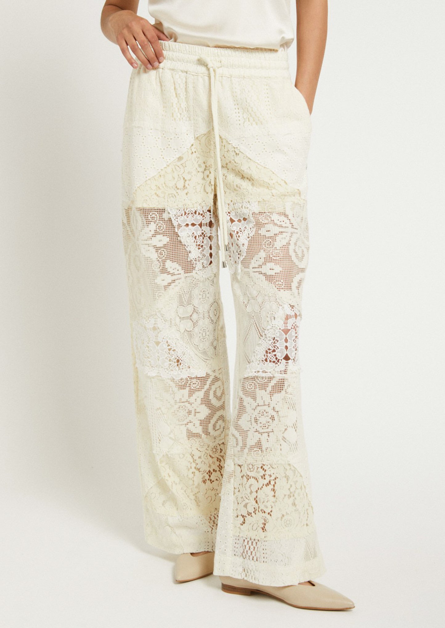 A woman wearing a pair of patchwork lace pants in cream.