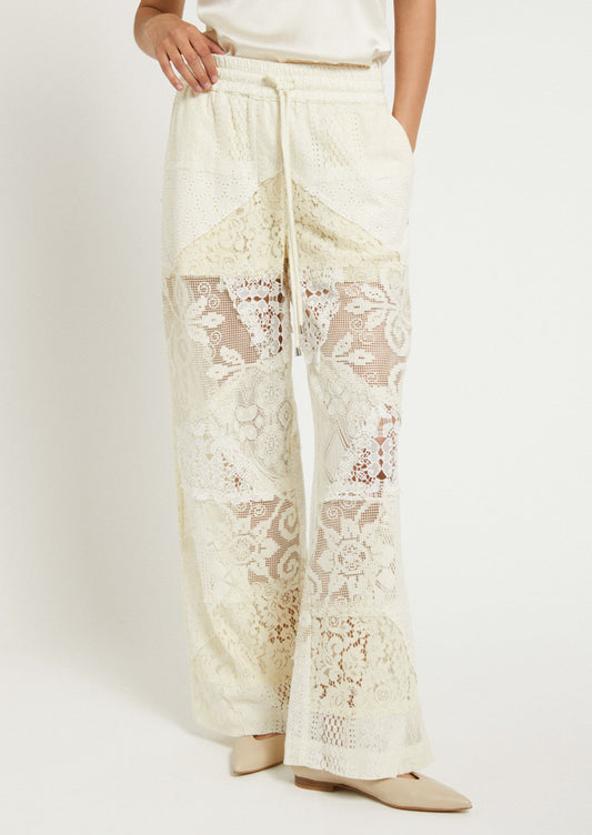 A woman wearing a pair of patchwork lace pants in cream.