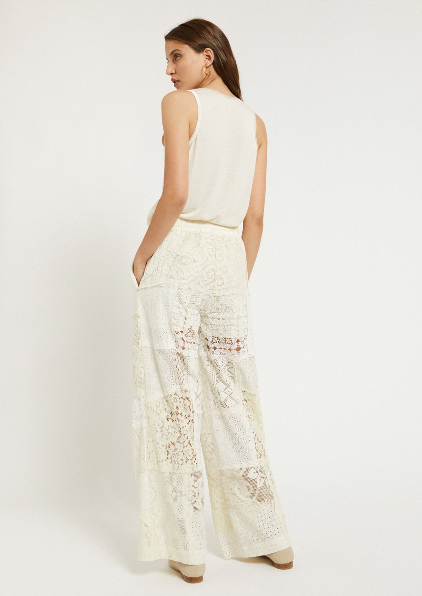 A woman wearing a pair of patchwork lace pants in cream.