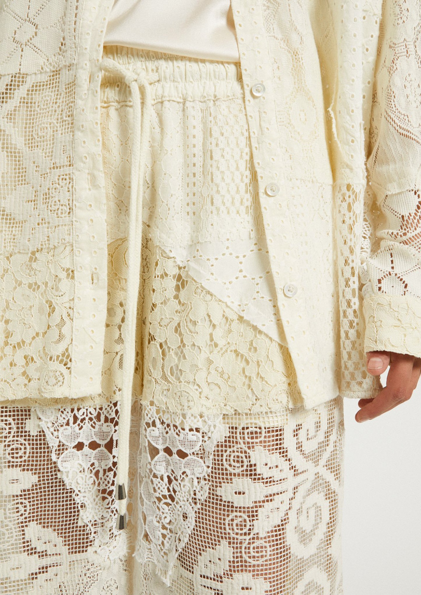 A woman wearing a pair of patchwork lace pants in cream.