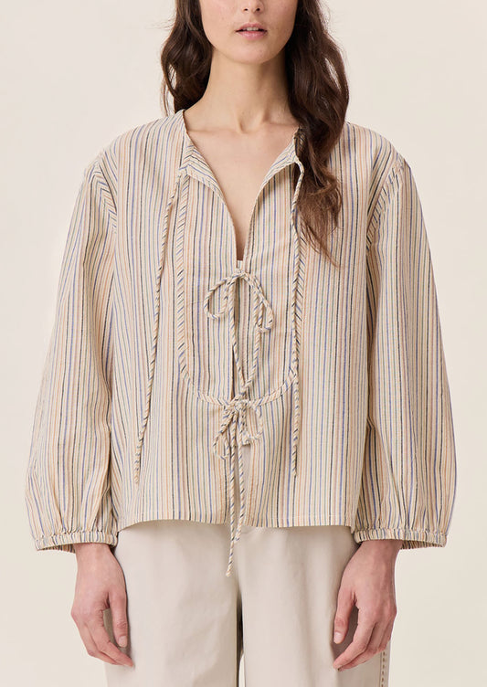 A woman wearing a tie neck blouse in cream with pastel multicolor stripe pattern.