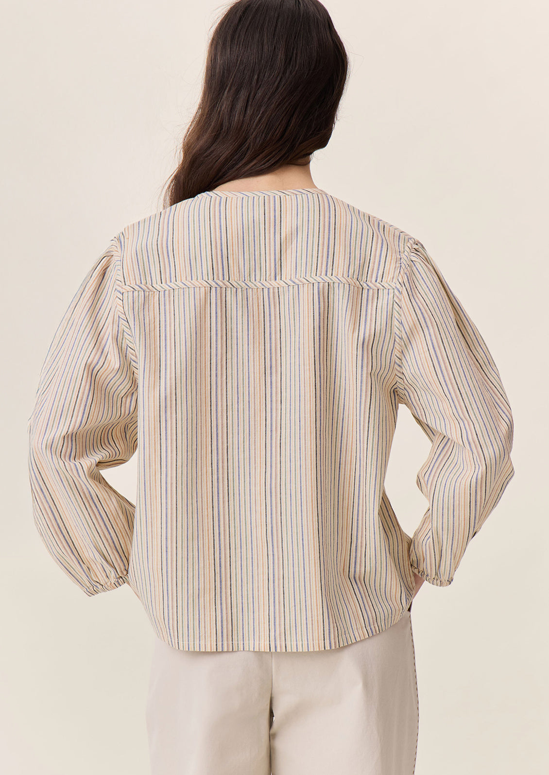A woman wearing a tie neck blouse in cream with pastel multicolor stripe pattern.