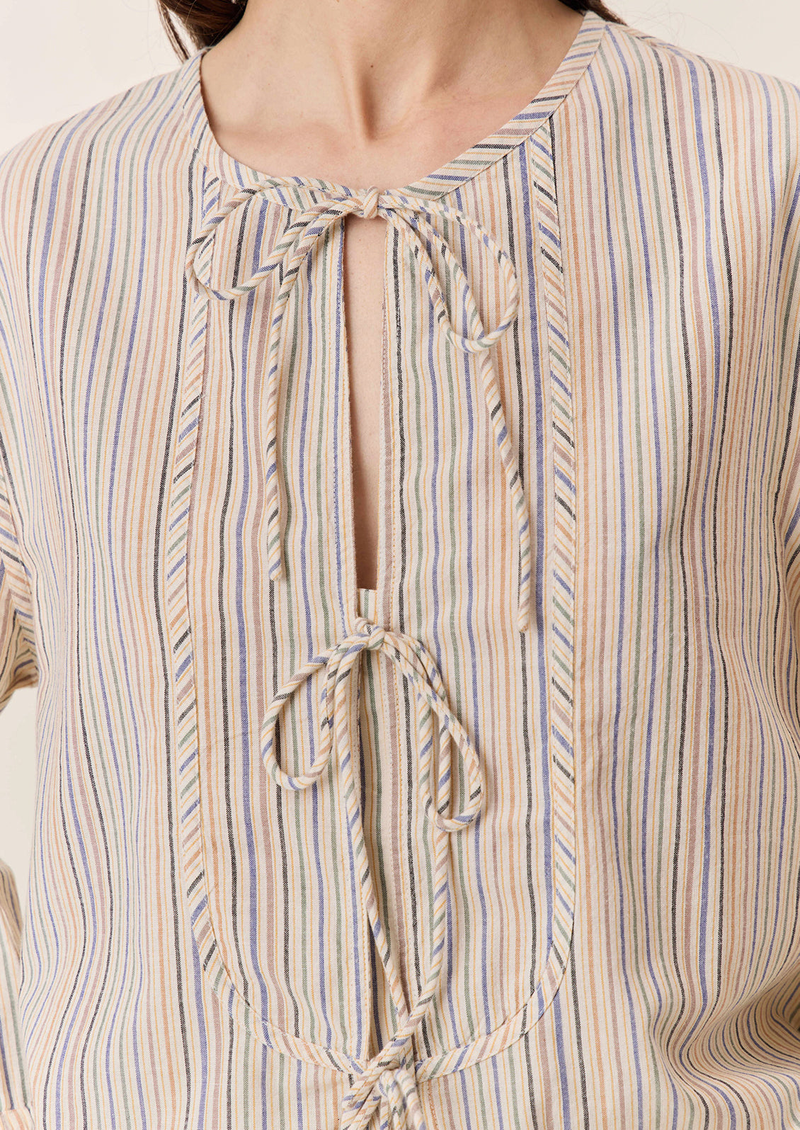 A woman wearing a tie neck blouse in cream with pastel multicolor stripe pattern.