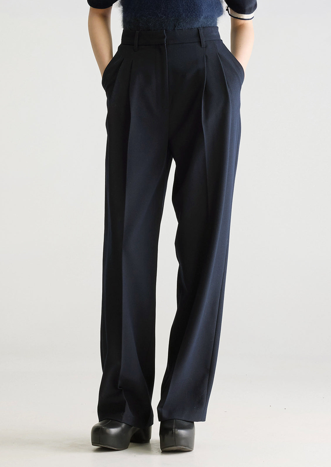 A person wearing a pair of navy blue dress trousers with pleated front.