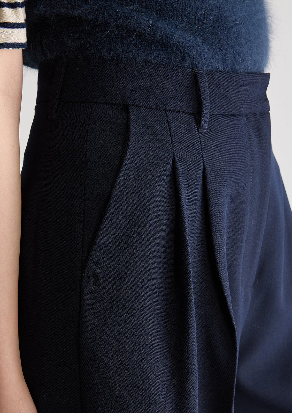 A person wearing a pair of navy blue dress trousers with pleated front.