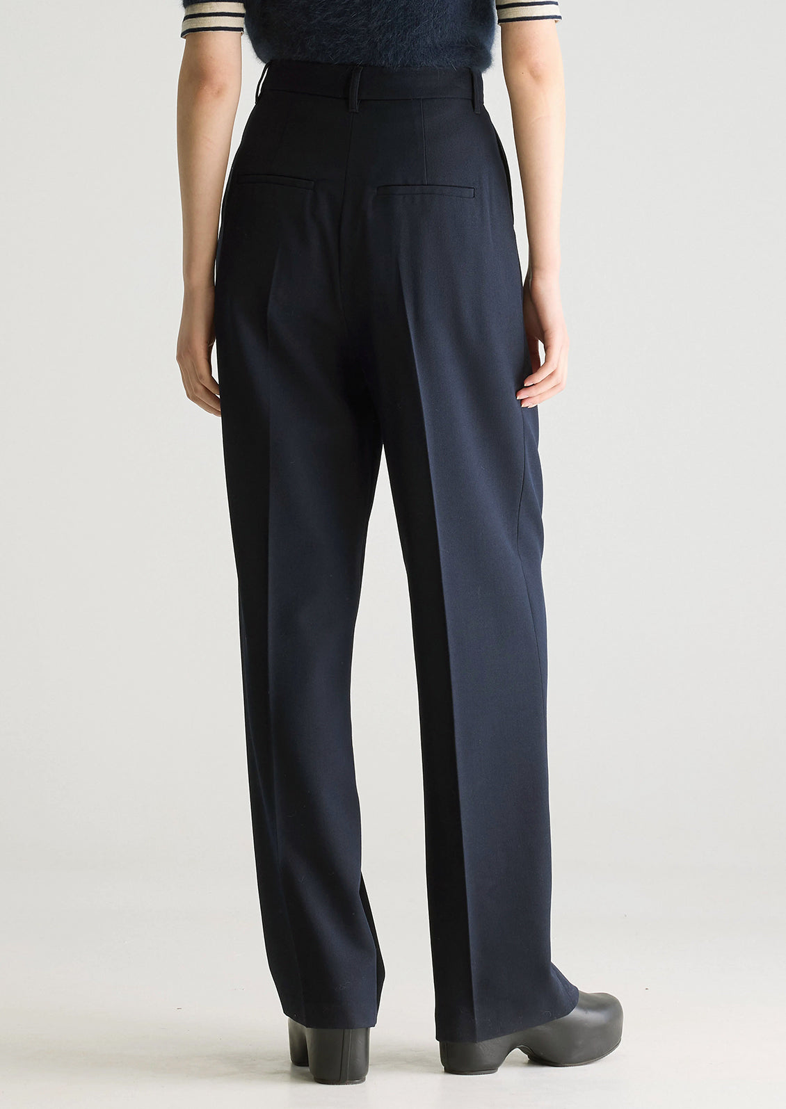 A person wearing a pair of navy blue dress trousers with pleated front.