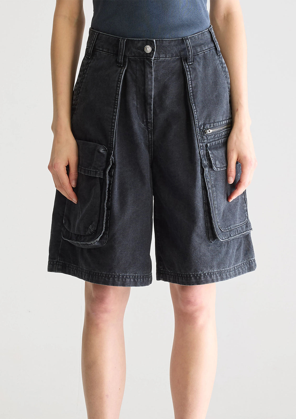 A person wearing a pair of charcoal denim cargo shorts.