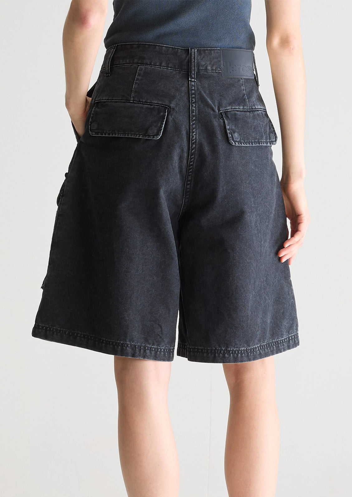 A person wearing a pair of charcoal denim cargo shorts.