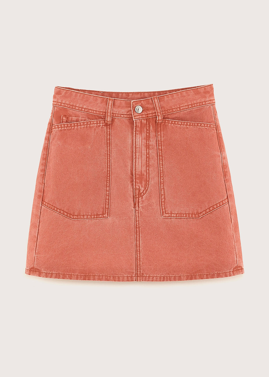 A person wearing a mini skirt in coral colored denim.