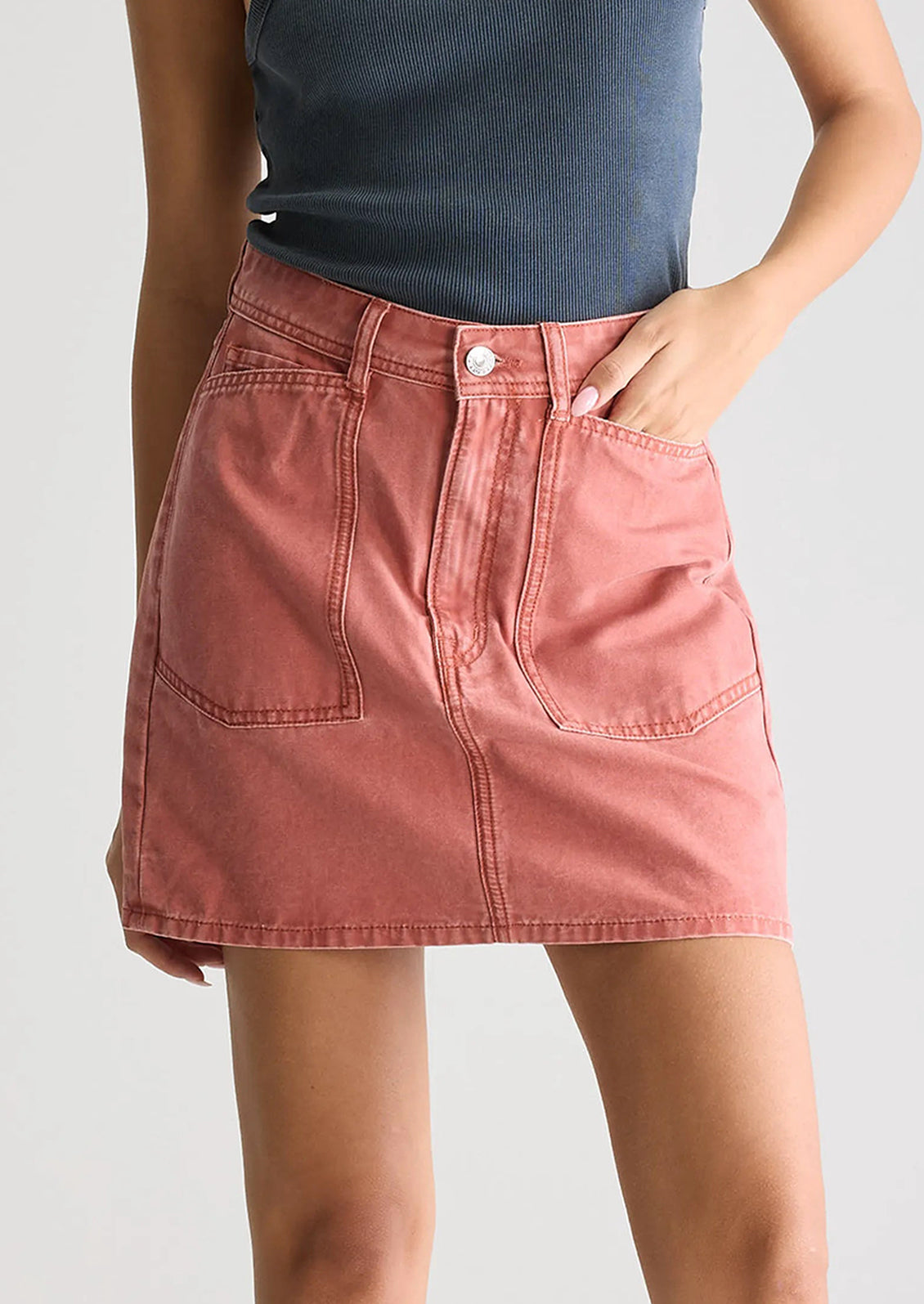 A person wearing a mini skirt in coral colored denim.