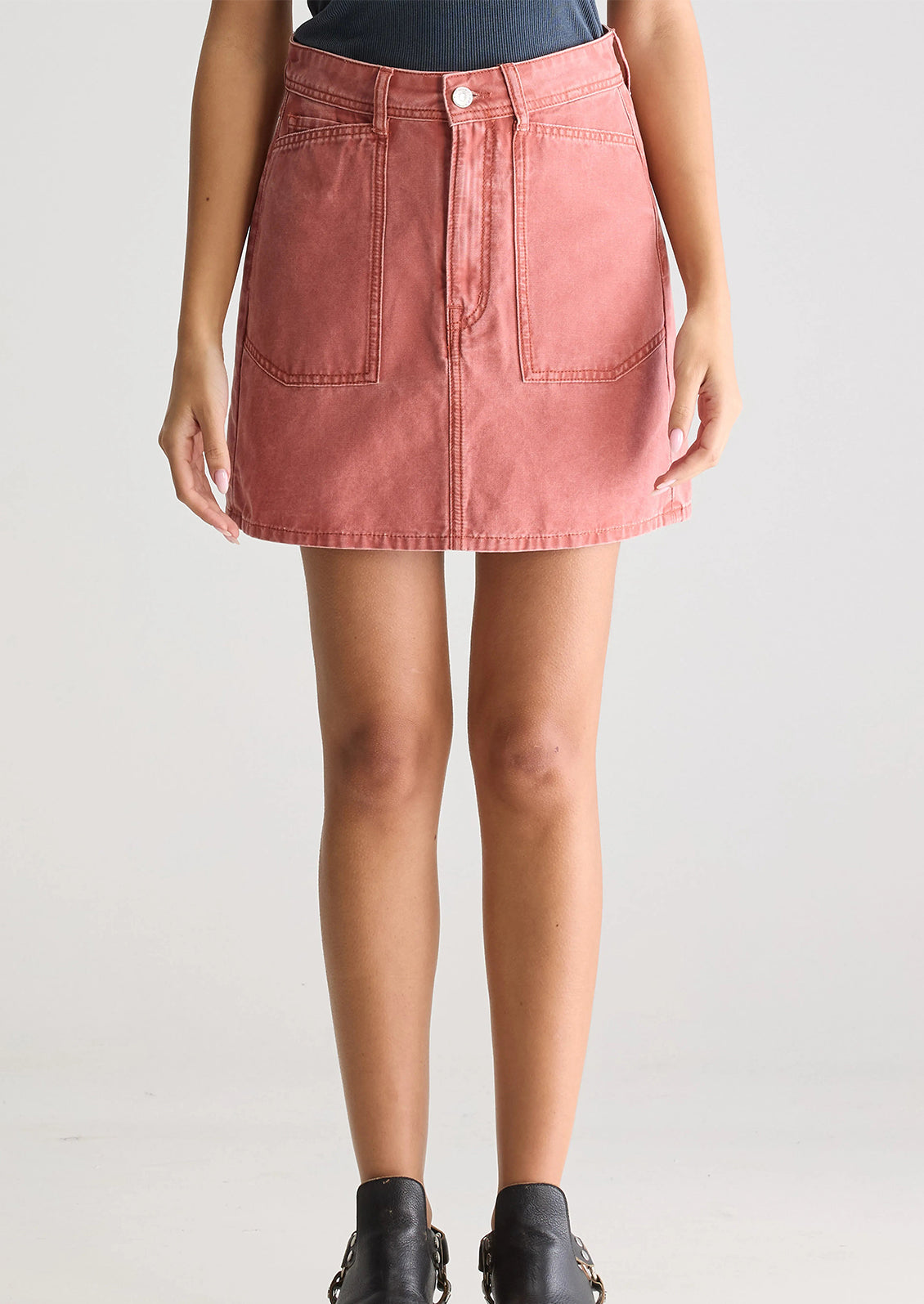 A person wearing a mini skirt in coral colored denim.