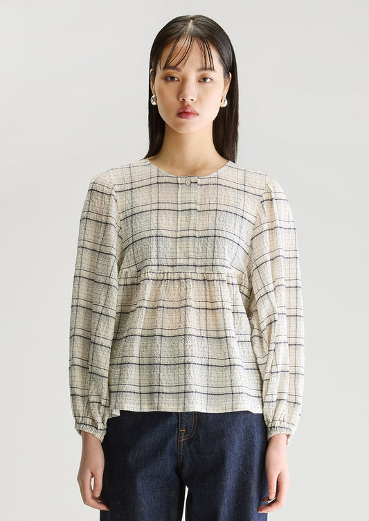 A woman wearing a crinkly textured blouse in ivory with navy check pattern.