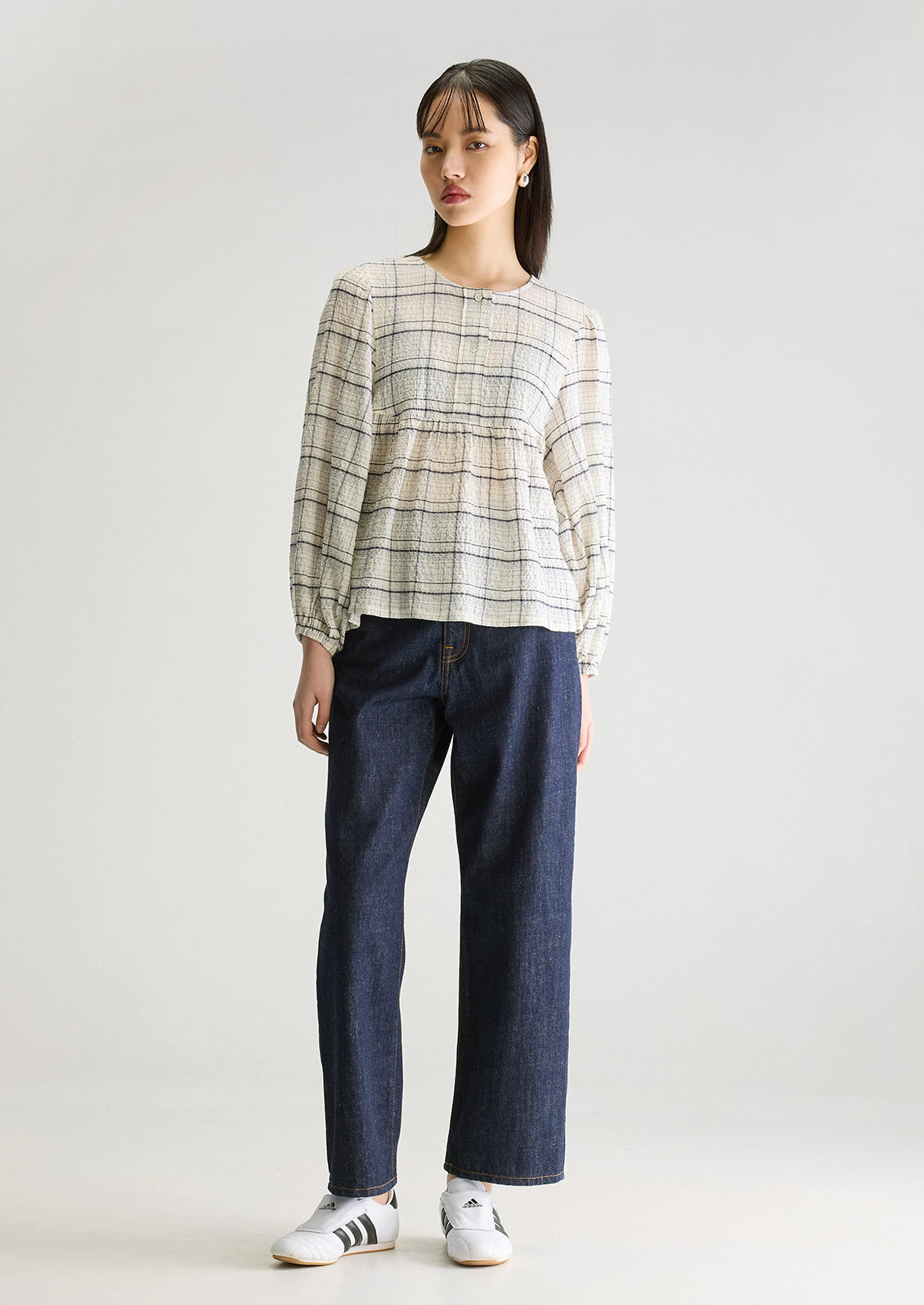 A woman wearing a crinkly textured blouse in ivory with navy check pattern.