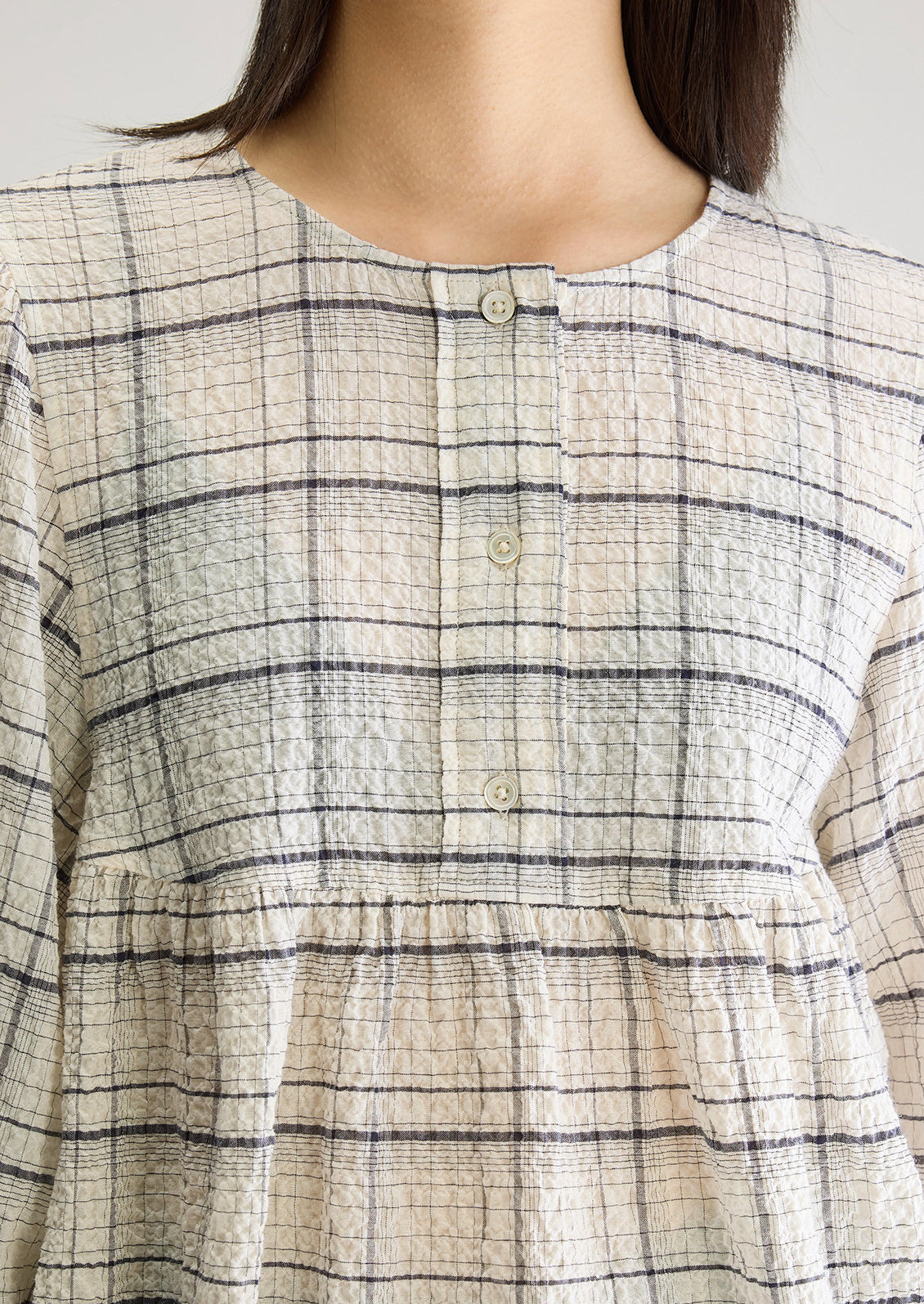 A woman wearing a crinkly textured blouse in ivory with navy check pattern.