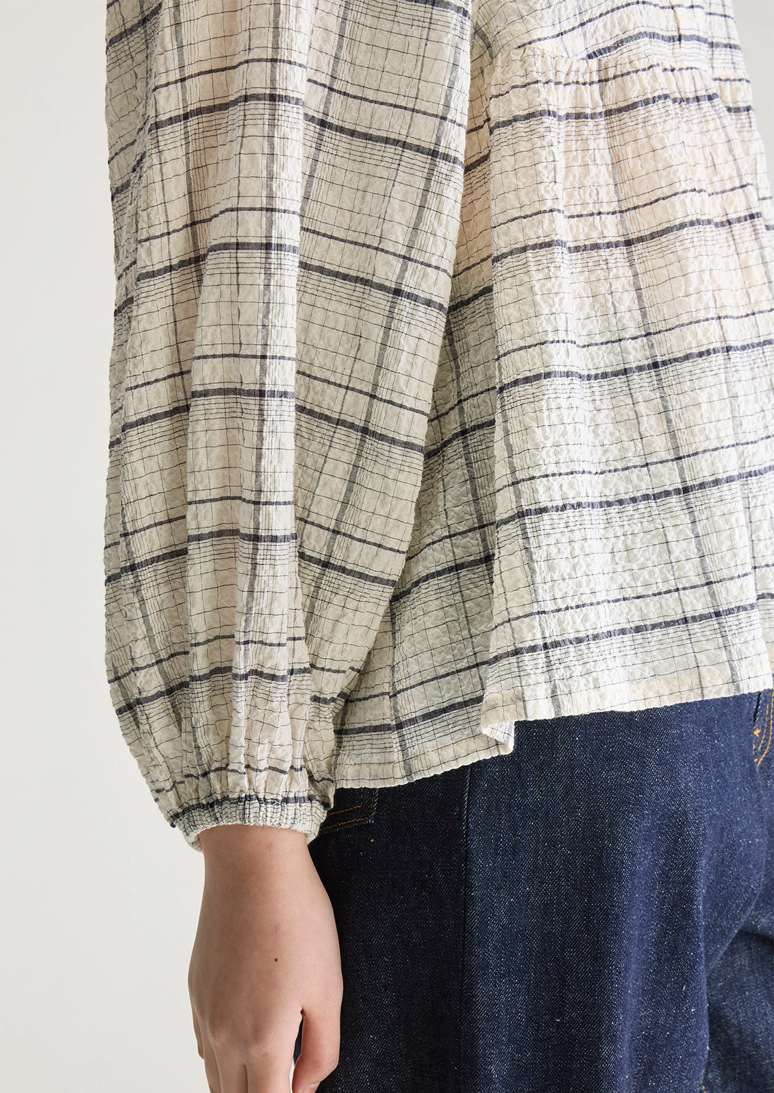 A woman wearing a crinkly textured blouse in ivory with navy check pattern.