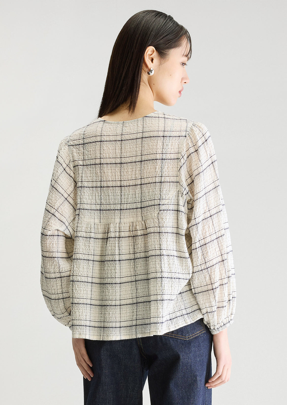 A woman wearing a crinkly textured blouse in ivory with navy check pattern.