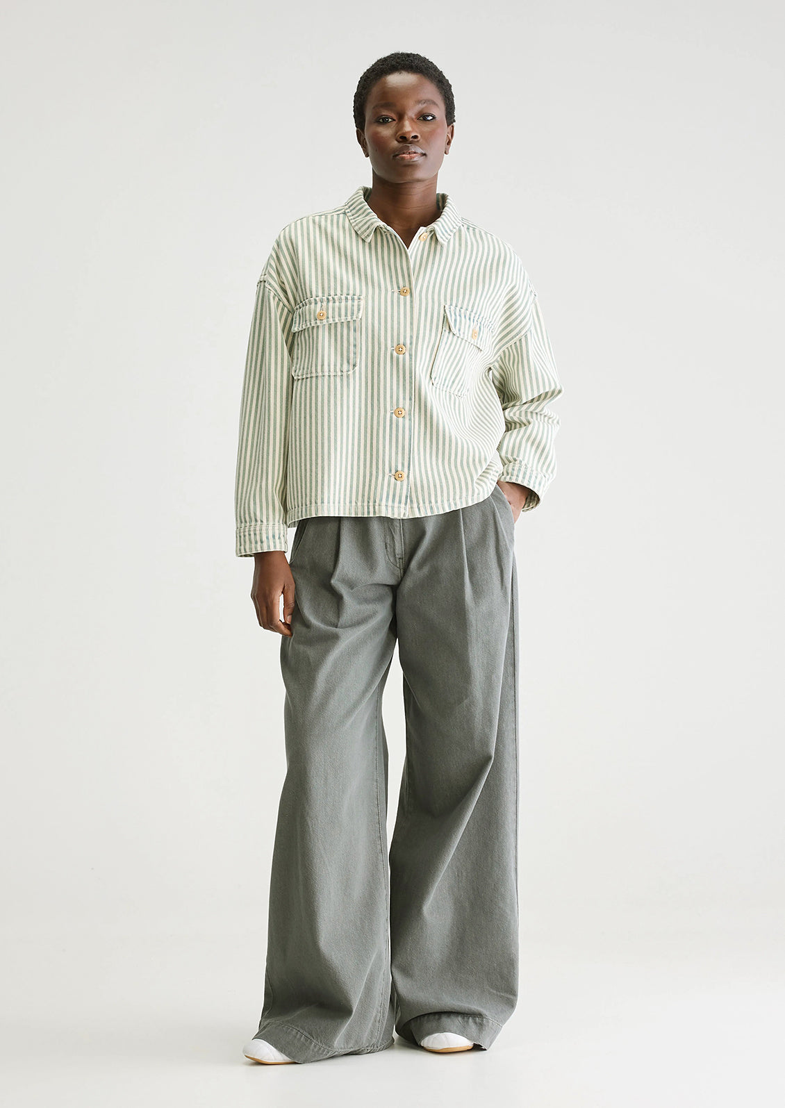 A woman wearing a striped overshirt in cream and acid dye blue/green.