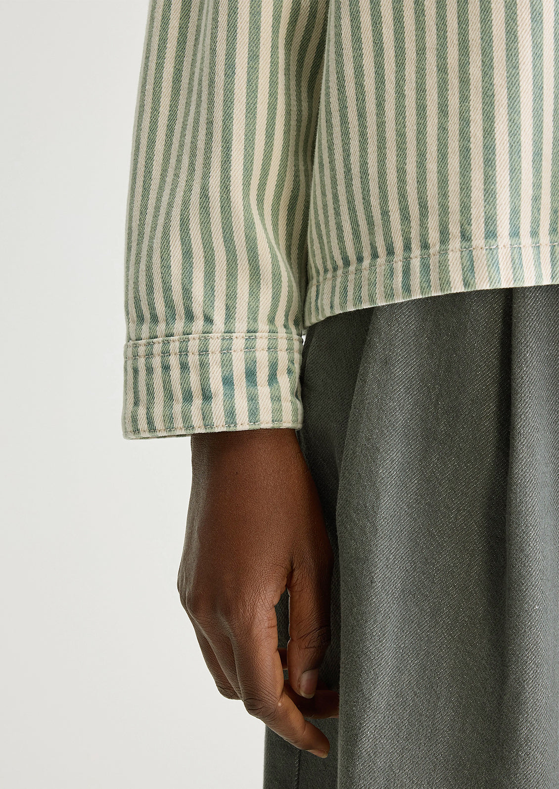 A woman wearing a striped overshirt in cream and acid dye blue/green.
