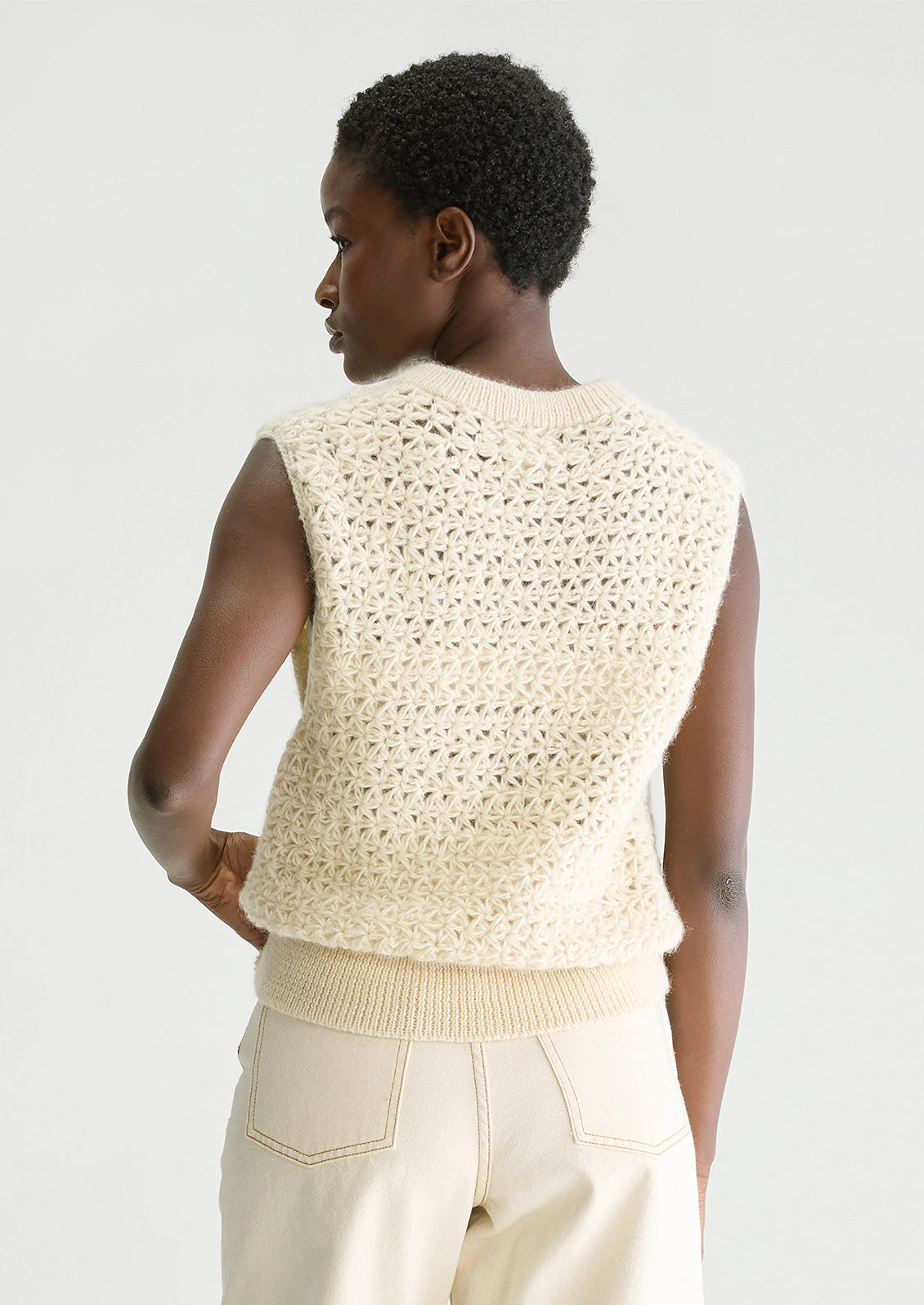 A woman wearing a sleeveless crewneck sweater vest in triangular open weave wool.