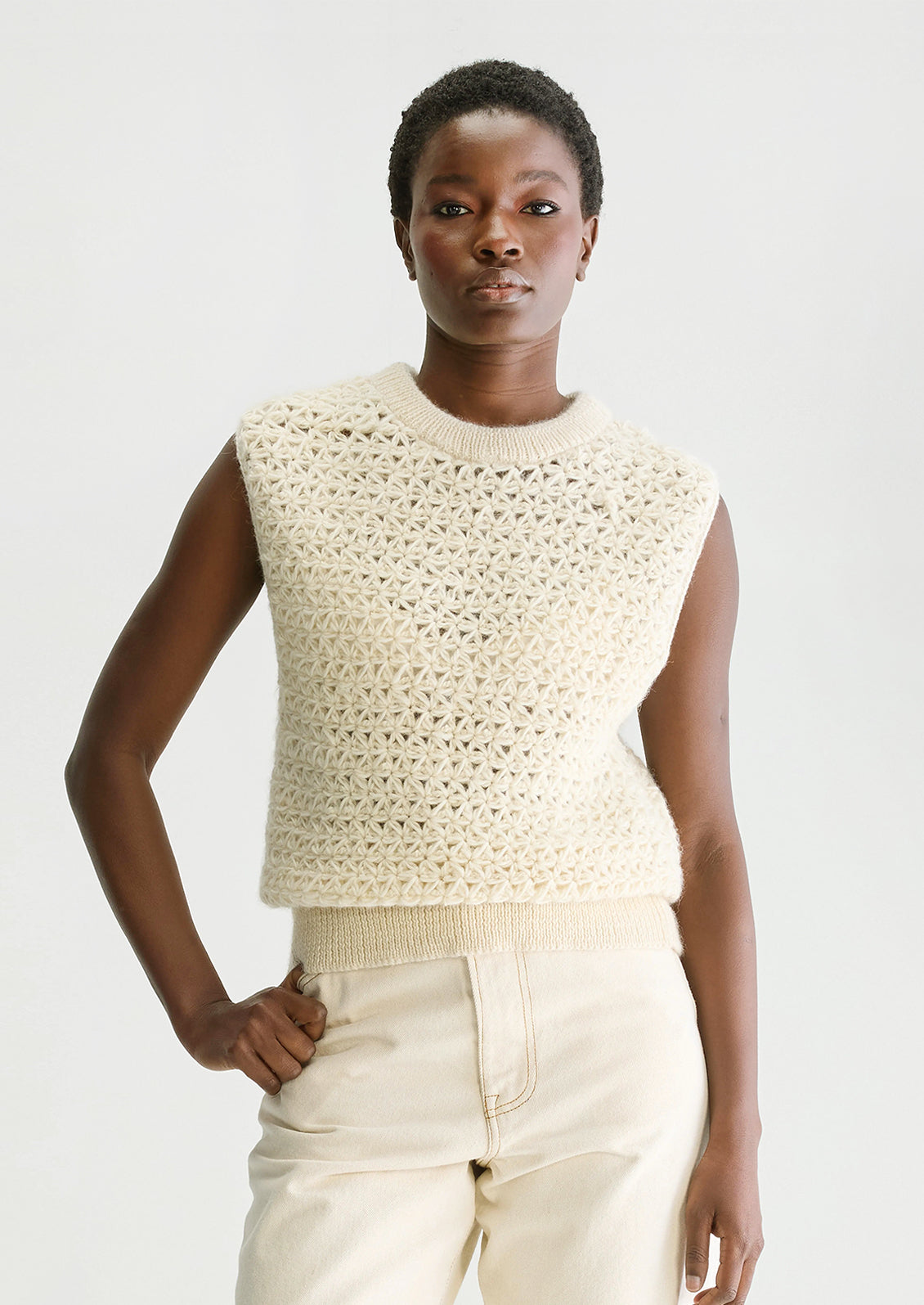 A woman wearing a sleeveless crewneck sweater vest in triangular open weave wool.