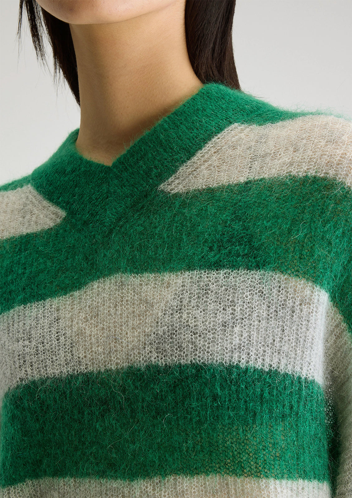A woman wearing a mohair sweater in green and grey big stripes, with high v-neck.