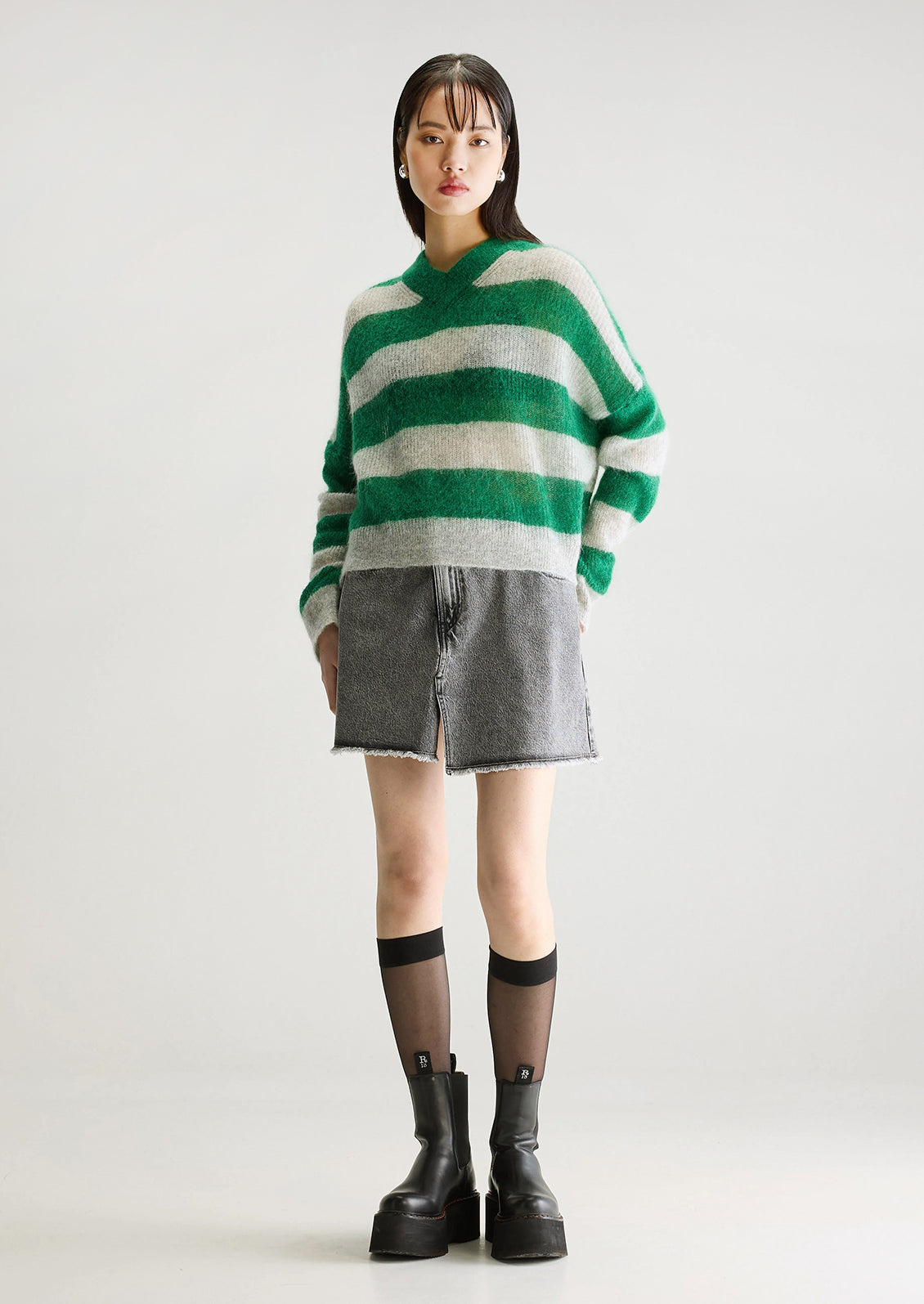 A woman wearing a mohair sweater in green and grey big stripes, with high v-neck.