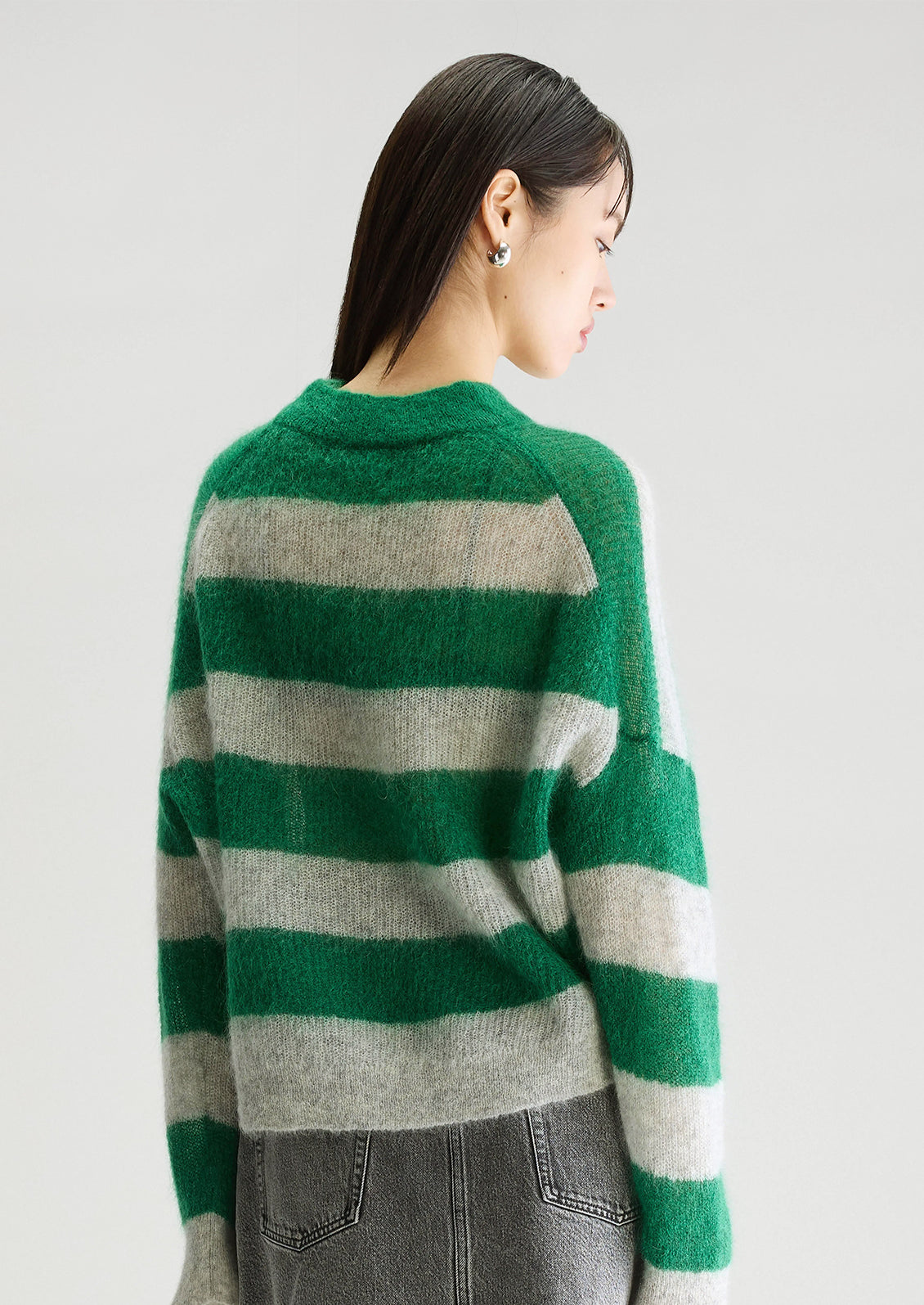 A woman wearing a mohair sweater in green and grey big stripes, with high v-neck.