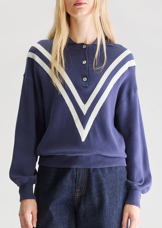 A woman wearing a navy blue henley long sleeve polo with inset V-shaped contrast detailing.