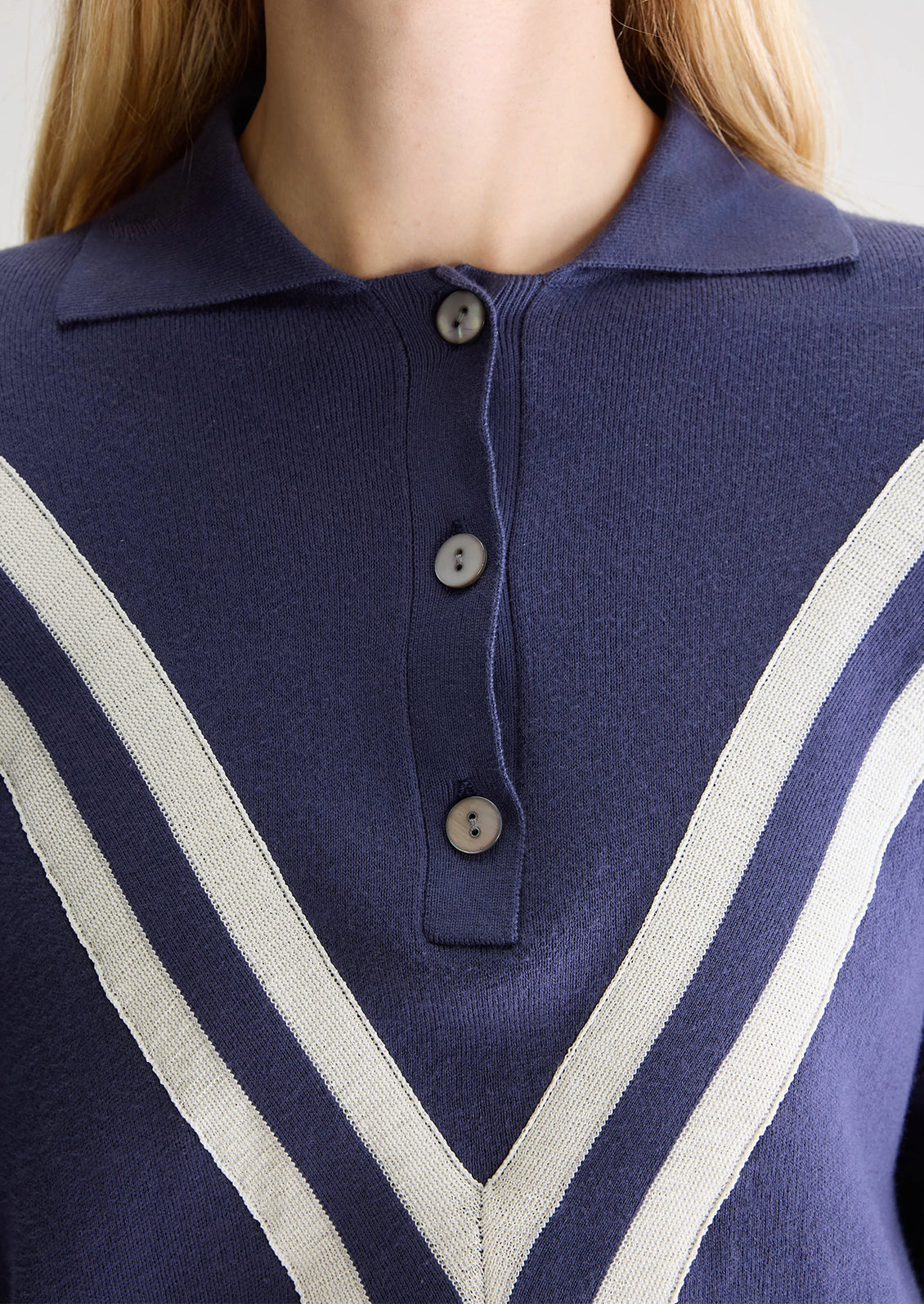 A woman wearing a navy blue henley long sleeve polo with inset V-shaped contrast detailing.