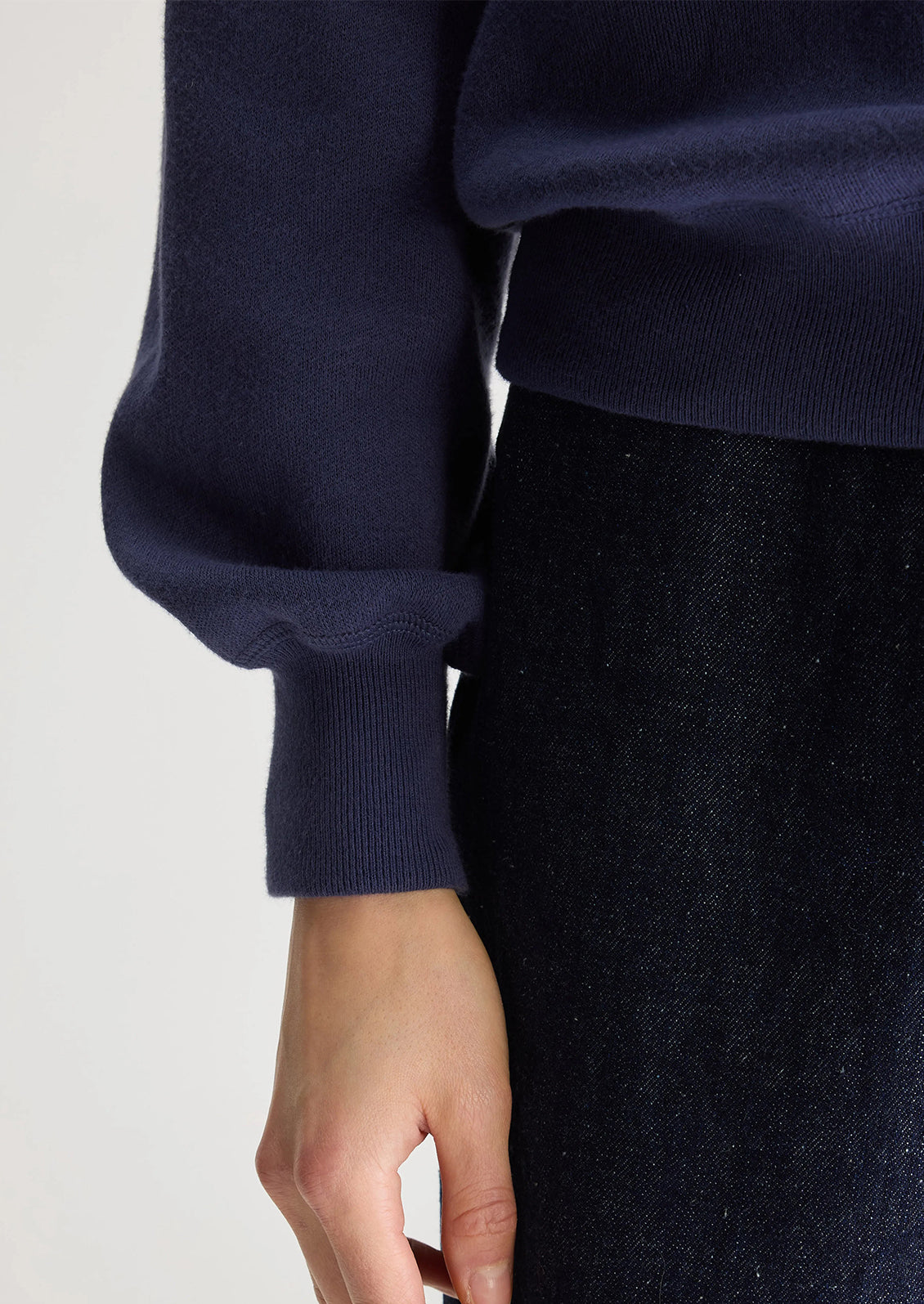 A woman wearing a navy blue henley long sleeve polo with inset V-shaped contrast detailing.