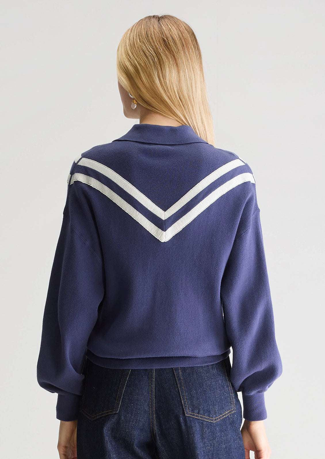 A woman wearing a navy blue henley long sleeve polo with inset V-shaped contrast detailing.