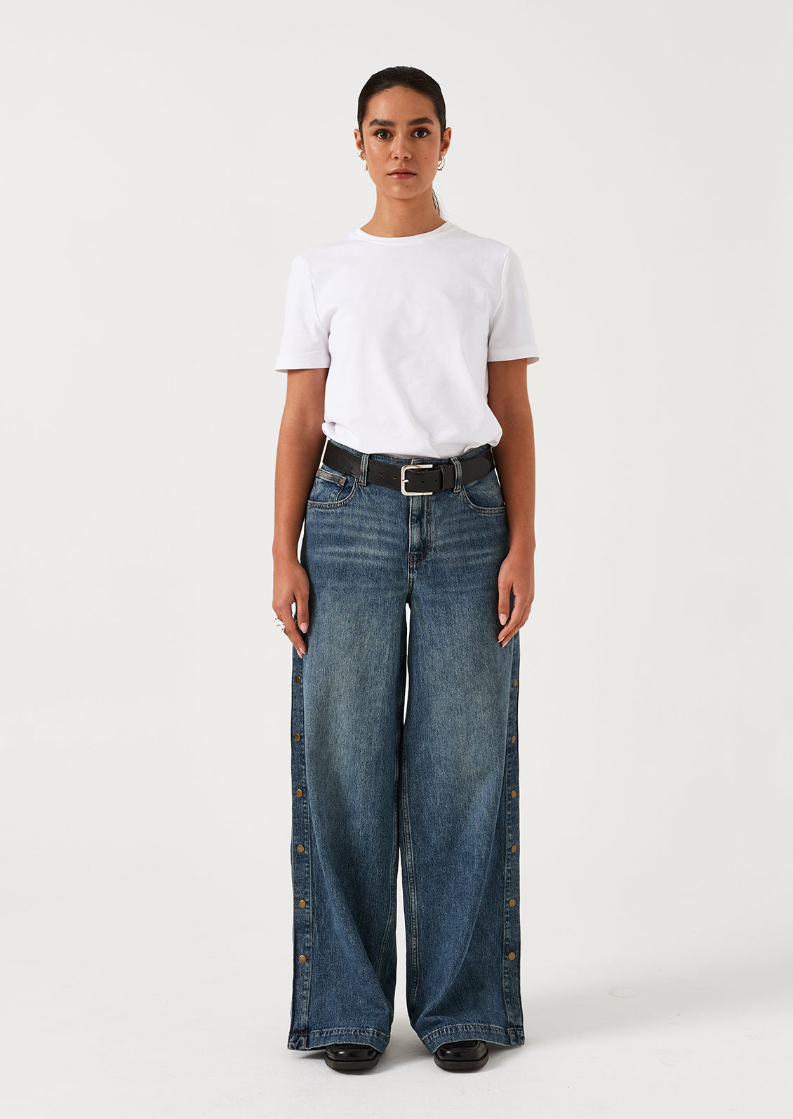 A woman wearing a pair of medium blue denim wide leg jeans with windbreaker-style snap detail along outer leg.