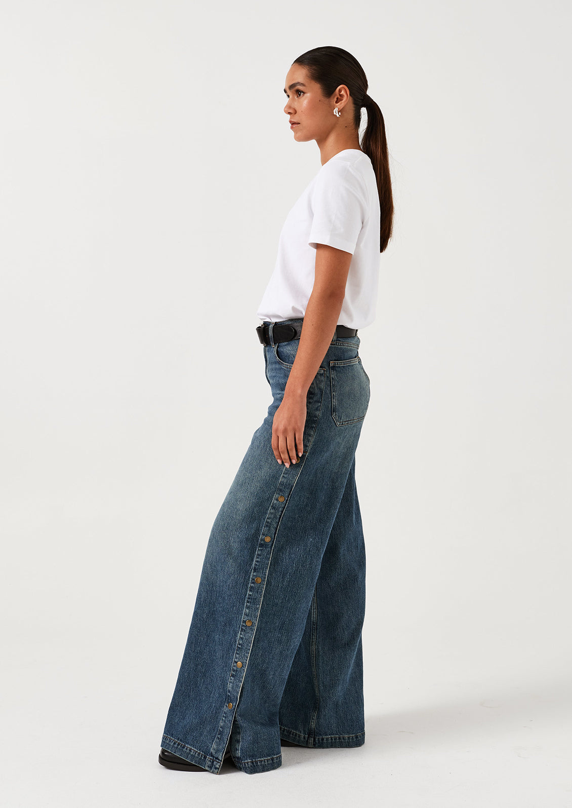 A woman wearing a pair of medium blue denim wide leg jeans with windbreaker-style snap detail along outer leg.