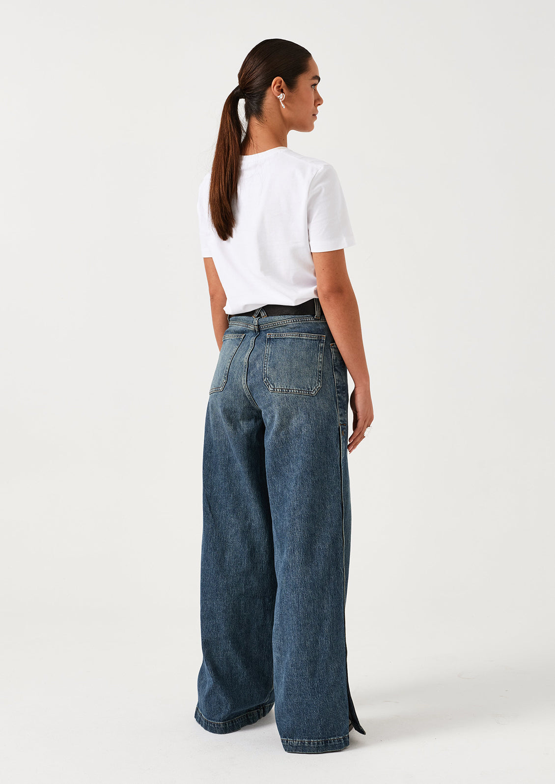 A woman wearing a pair of medium blue denim wide leg jeans with windbreaker-style snap detail along outer leg.