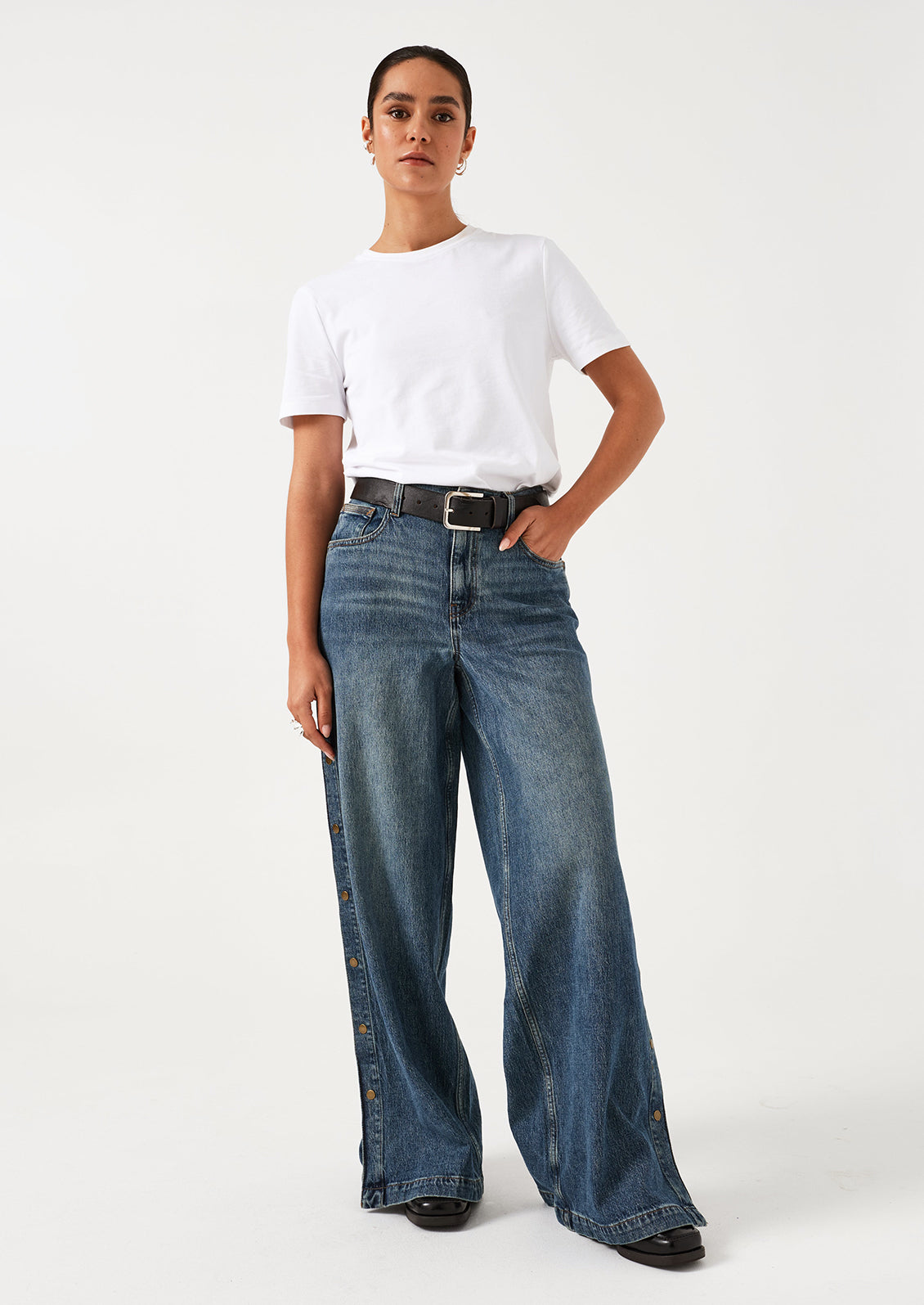 A woman wearing a pair of medium blue denim wide leg jeans with windbreaker-style snap detail along outer leg.