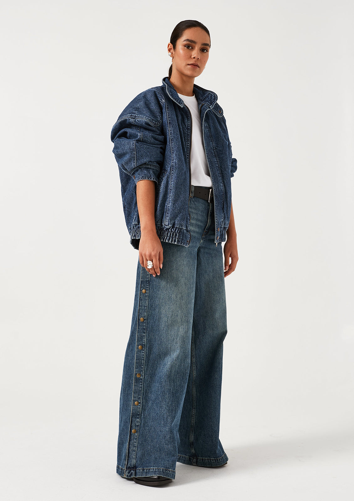 A woman wearing a pair of denim wide leg jeans with windbreaker-style snap detail along outer leg.