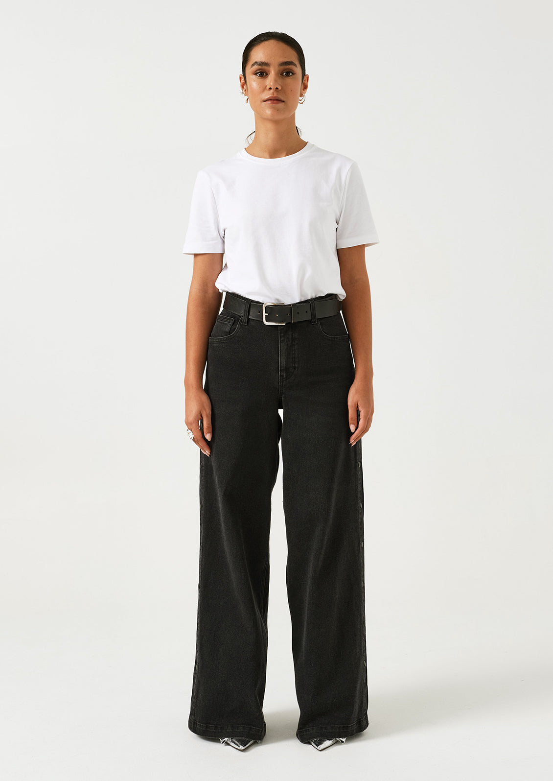 A woman wearing a pair of black wide leg jeans with windbreaker-style snap detail along outer leg.